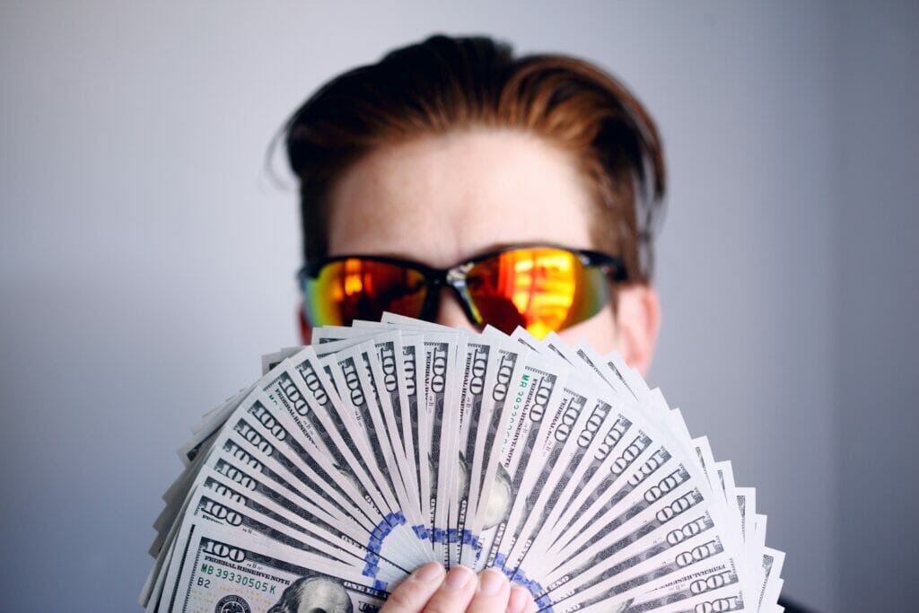 man with sunglasses holding up hundred dollar bills